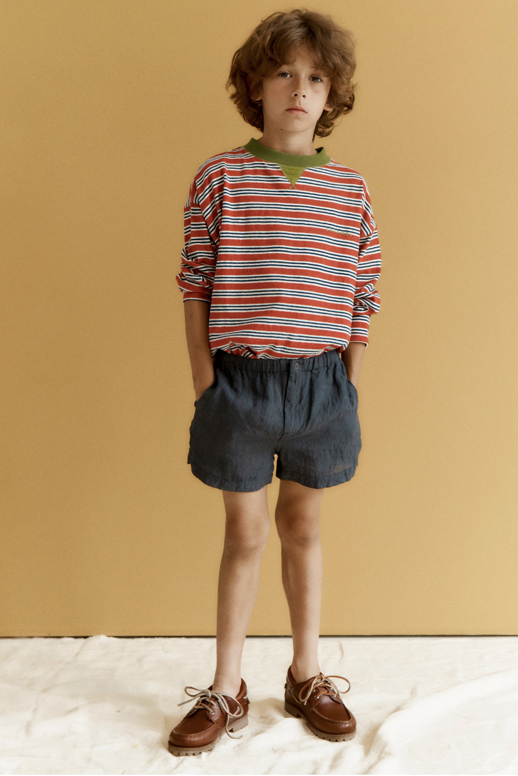 Child wearing a striped shirt and shorts against a beige background