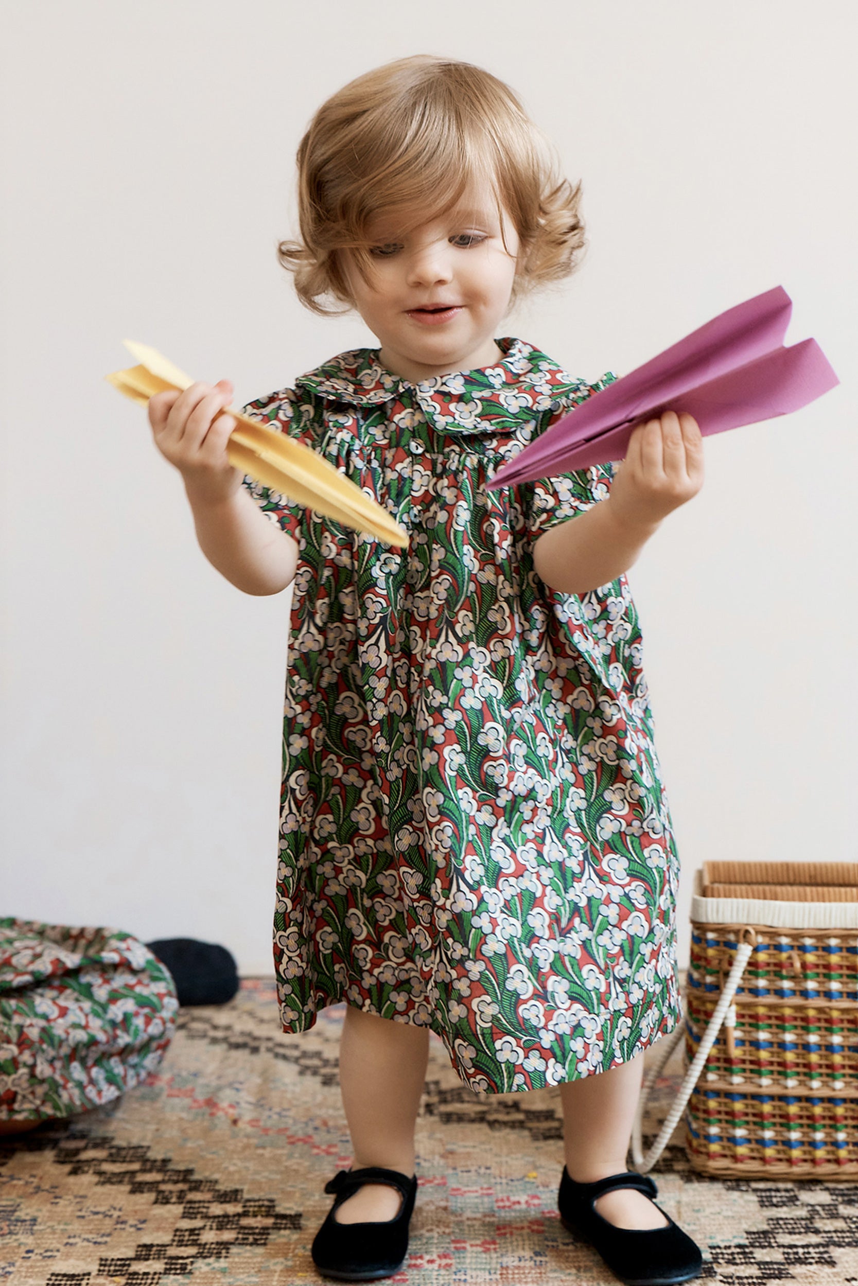 Child in a floral dress holding colorful paper planes against a neutral background
